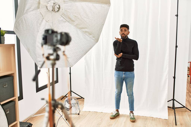 Young hispanic man with beard posing as model at photography studio looking at the camera blowing a kiss with hand on air being lovely and sexy. love expression.  - Photo, Image