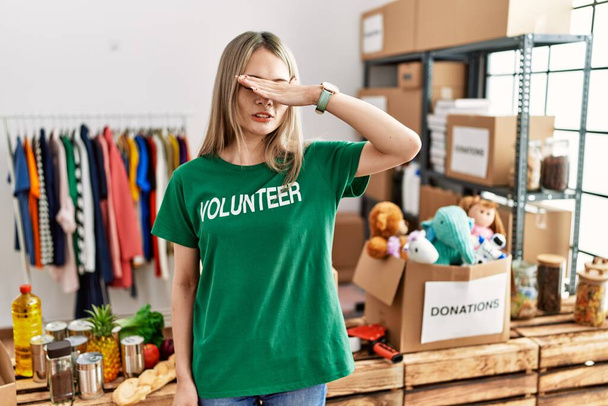 Asian young woman wearing volunteer t shirt at donations stand covering eyes with hand, looking serious and sad. sightless, hiding and rejection concept  - Photo, Image