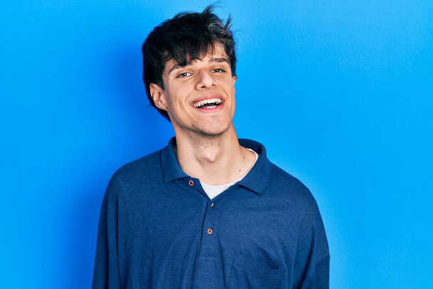 Handsome hipster young man stranding over blue background looking positive and happy standing and smiling with a confident smile showing teeth  - Photo, Image