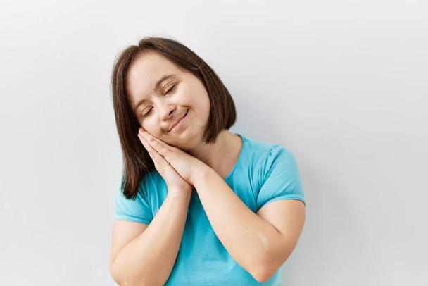 Młoda kobieta z zespołem Downa stojąca nad odosobnionym tłem śpiąca zmęczona snem i pozująca razem dłońmi, uśmiechnięta zamkniętymi oczami.  - Zdjęcie, obraz
