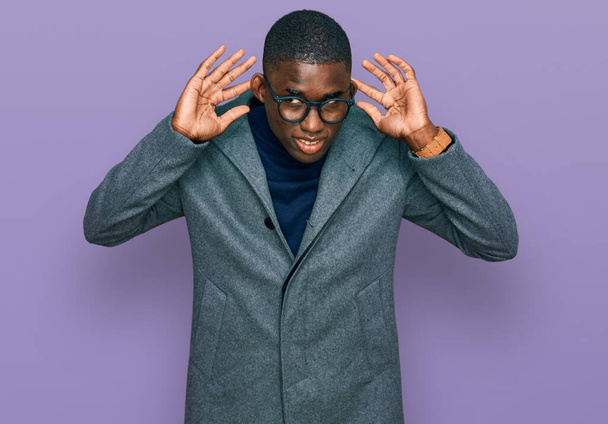 Junger afrikanisch-amerikanischer Mann in Businesskleidung und Brille, der versucht, beide Hände am Ohr zu hören, neugierig auf Klatsch. Hörprobleme, Gehörlosigkeit  - Foto, Bild
