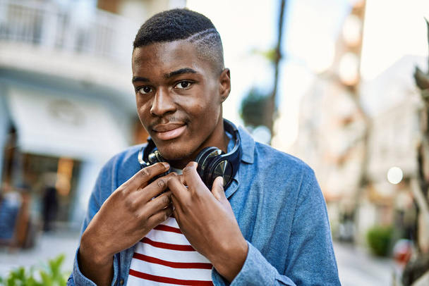 Jeune homme afro-américain souriant heureux en utilisant des écouteurs à la ville. - Photo, image