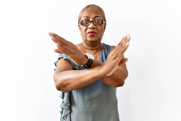 Mature hispanic woman wearing glasses standing over isolated background rejection expression crossing arms doing negative sign, angry face  - Photo, Image