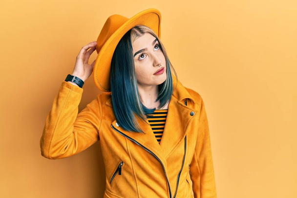 Młoda nowoczesna dziewczyna w żółtym kapeluszu i skórzanej kurtce myli i zastanawia się nad pytaniem. niepewny z wątpliwościami, myślący z ręką na głowie. zamyślona koncepcja.  - Zdjęcie, obraz