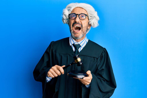 Middle age hispanic man using gavel angry and mad screaming frustrated and furious, shouting with anger looking up.  - Photo, Image