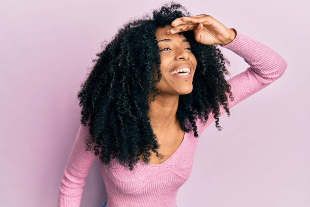 Afro-Amerikaanse vrouw met afro haar draagt casual roze shirt erg blij en glimlachend kijken ver weg met hand over hoofd. zoekconcept.  - Foto, afbeelding
