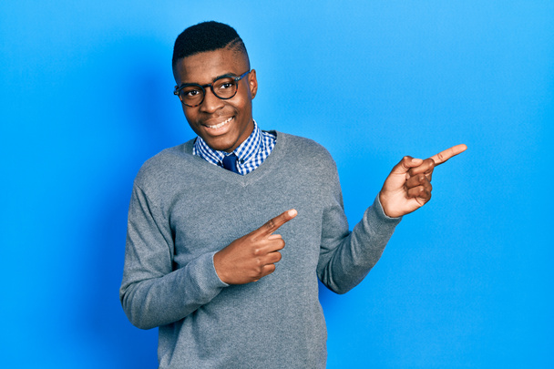 Junger afrikanisch-amerikanischer Mann mit Businessstil und Brille, der lächelnd in die Kamera blickt und mit zwei Händen und Fingern zur Seite zeigt.  - Foto, Bild
