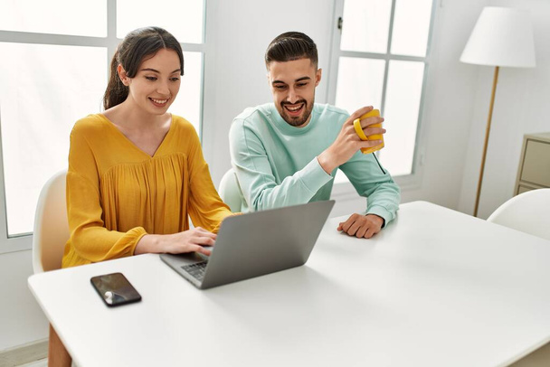 Giovane coppia ispanica utilizzando laptop e smartphone bere caffè a casa. - Foto, immagini