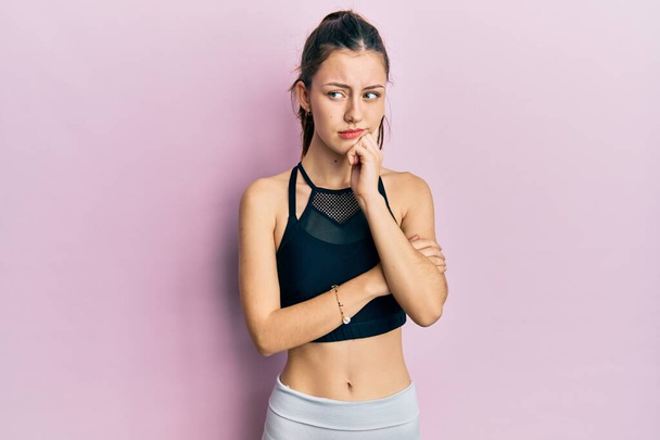 Young brunette woman wearing sportswear serious face thinking about question with hand on chin, thoughtful about confusing idea  - Photo, Image