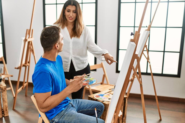 Student i nauczyciel uśmiechający się szczęśliwy malarstwo w szkole artystycznej. - Zdjęcie, obraz