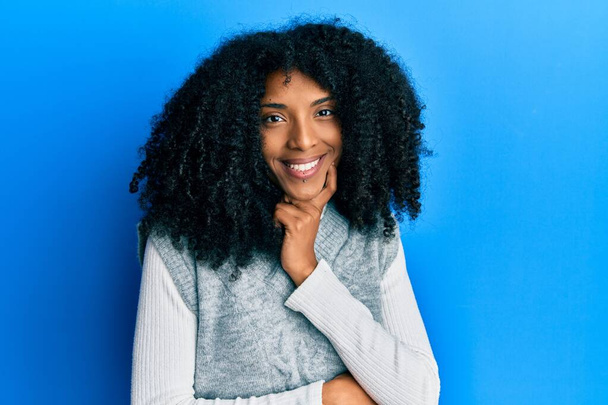 Afrikai amerikai nő afro hajjal, alkalmi téli pulóvert visel, magabiztosan néz a kamerába, keresztbe tett karral és felemelt kézzel mosolyog. pozitív gondolkodás.  - Fotó, kép