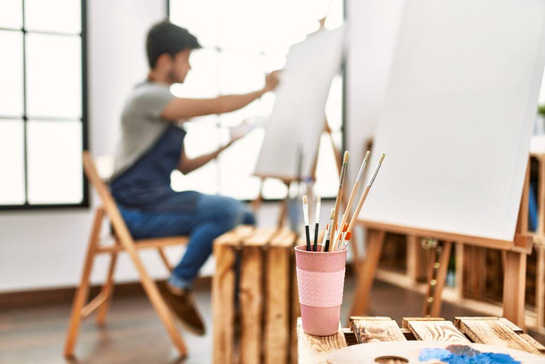 Jovem artista hispânico homem sorrindo pintura feliz no estúdio de arte. - Foto, Imagem