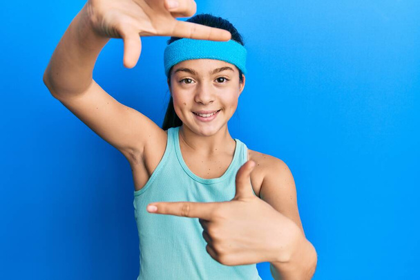 Beautiful brunette little girl wearing sportswear and diadem smiling making frame with hands and fingers with happy face. creativity and photography concept.  - Photo, Image