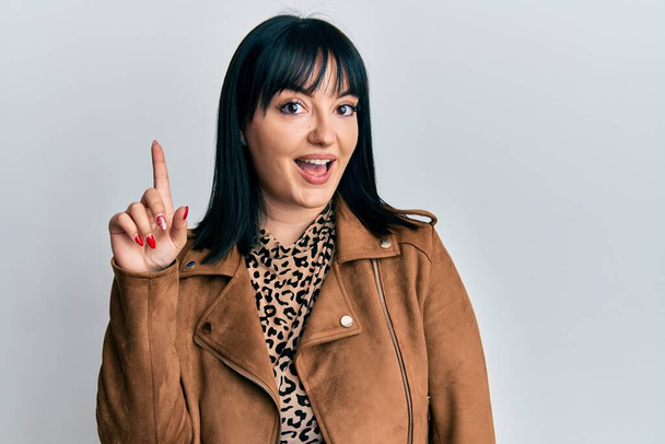 Young hispanic woman wearing casual leather jacket smiling with an idea or question pointing finger up with happy face, number one  - Photo, Image
