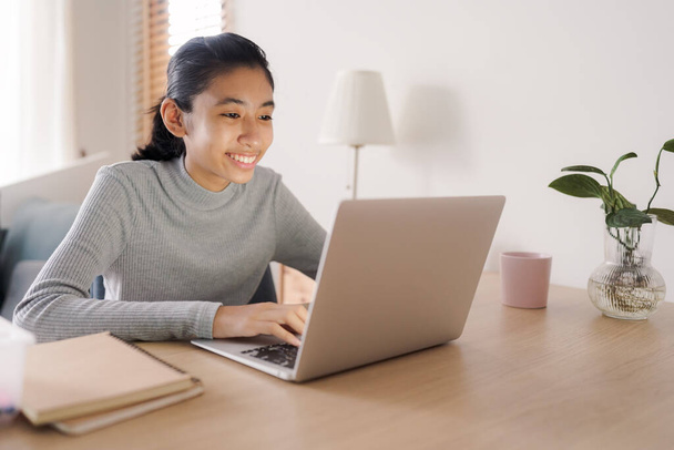 Asian woman using laptop typing work on a table at home, Asia student happy smile while learn online via internet on a computer, Concept online learning at home  - Φωτογραφία, εικόνα