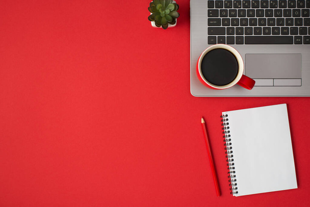 Overhead-Foto von Laptop-Pflanze Tasse Kaffee Notizblock und Bleistift isoliert auf dem roten Hintergrund mit leerem Raum - Foto, Bild