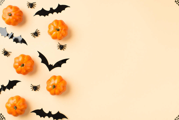 Top view photo of halloween decorations small pumpkins web in the corners spiders and bats silhouettes on isolated beige background with empty space - Foto, imagen