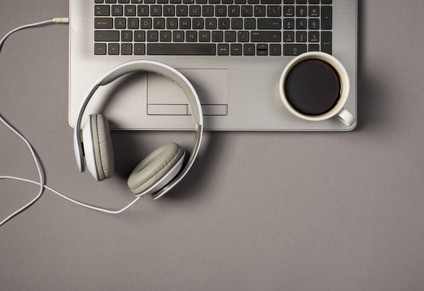 Widok z góry zdjęcie przewodowych białych słuchawek i filiżanka kawy na klawiaturze laptopa na izolowanym szarym tle - Zdjęcie, obraz