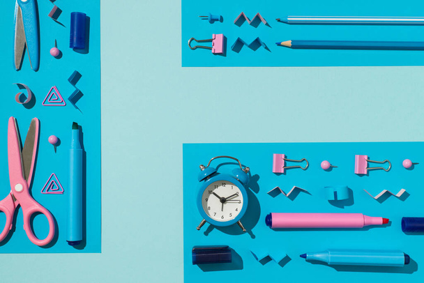 Top view photo of ordered composition bicolor blue and pink school supplies stationery markers pen pencil binder clips pins scissors and alarm clock on isolated light blue background with empty space - Foto, afbeelding