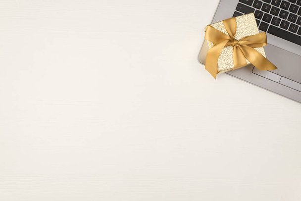 Widok z góry zdjęcie białego i złotego pudełeczka ze złotą wstążką na laptopie na izolowanym białym drewnianym tle z copyspace - Zdjęcie, obraz