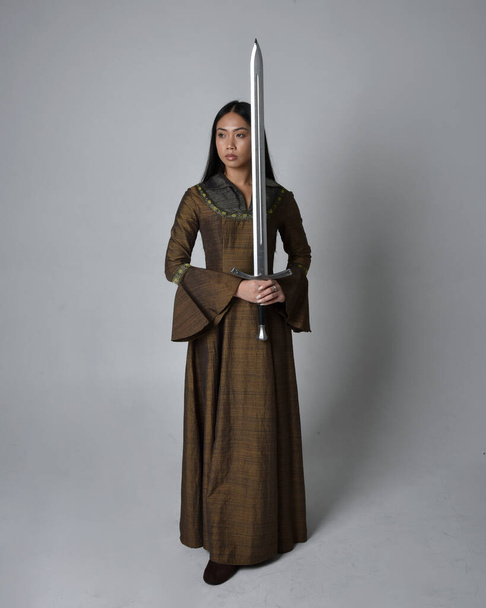 Plná délka portrét krásné mladé asijské ženy s dlouhými vlasy na sobě středověké fantasy šaty kostým. Půvabné stojící pózování s mečem, izolované na pozadí studia. - Fotografie, Obrázek