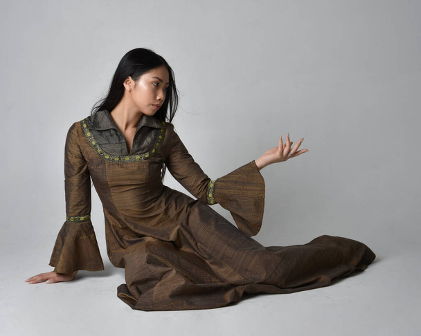 Retrato de larga duración de una hermosa mujer asiática joven con el pelo largo con traje de vestido de fantasía medieval. pose sentada agraciada, aislado en el fondo del estudio. - Foto, imagen