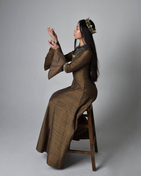 Portrait pleine longueur de belle jeune femme asiatique aux cheveux longs portant robe fantaisie médiévale et costume de couronne d'or. pose assise gracieuse, isolée sur fond de studio. - Photo, image
