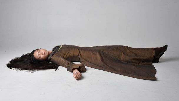 Ganzes Porträt einer schönen jungen asiatischen Frau mit langen Haaren, die ein mittelalterliches Fantasiegewand trägt. Anmutige Schlafpose, isoliert auf Studiohintergrund. - Foto, Bild