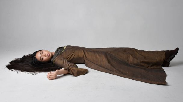 Teljes hosszúságú portré gyönyörű, fiatal ázsiai nőről, hosszú hajjal, középkori álomruhában. Kecses alvó póz, elszigetelt stúdió háttér. - Fotó, kép