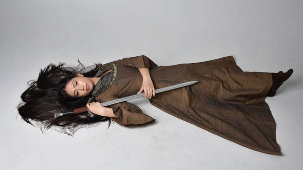 Πλήρες πορτρέτο της όμορφης νεαρής Ασιάτισσας με μακριά μαλλιά που φοράει μεσαιωνικό φόρεμα φαντασίας. Χαριτωμένη στάση ύπνου, απομονωμένη σε στούντιο φόντο. - Φωτογραφία, εικόνα