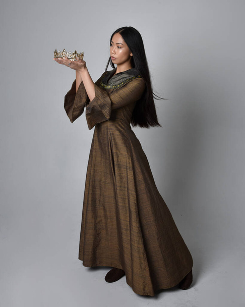 Πλήρες πορτρέτο της όμορφης νεαρής Ασιάτισσας με μακριά μαλλιά που φοράει μεσαιωνικό φόρεμα φαντασίας και χρυσό στέμμα. Χαριτωμένη στάση πόζα, απομονωμένη σε φόντο στούντιο. - Φωτογραφία, εικόνα