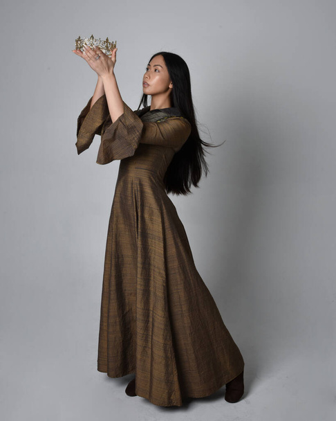 Полный портрет красивой молодой азиатской женщины с длинными волосами в средневековом фэнтези-платье и золотой короне. Изящная поза, изолированная на фоне студии. - Фото, изображение