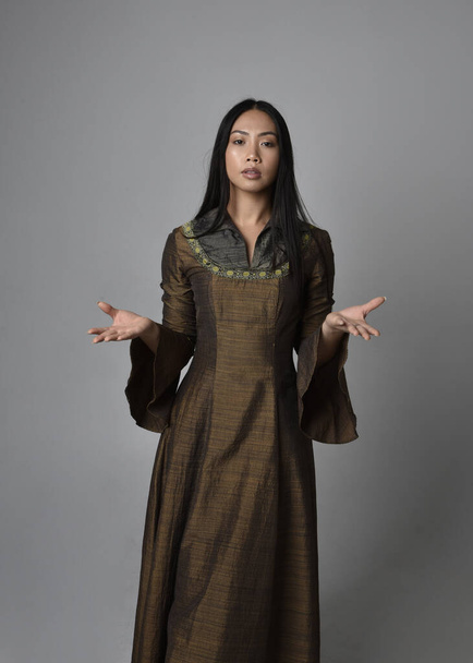 Крупный план портрета красивой молодой азиатской женщины с длинными волосами в средневековом фэнтези-платье. Изящная поза с жестикулирующими руками, изолированная на фоне студии. - Фото, изображение