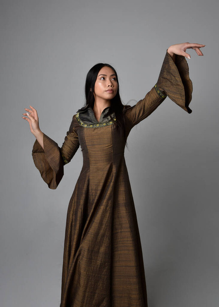 Orta çağ fantezi elbisesi giymiş, uzun saçlı güzel Asyalı bir kadının portresi. Hareketli elleri olan zarif bir poz, stüdyo arka planında izole edilmiş.. - Fotoğraf, Görsel