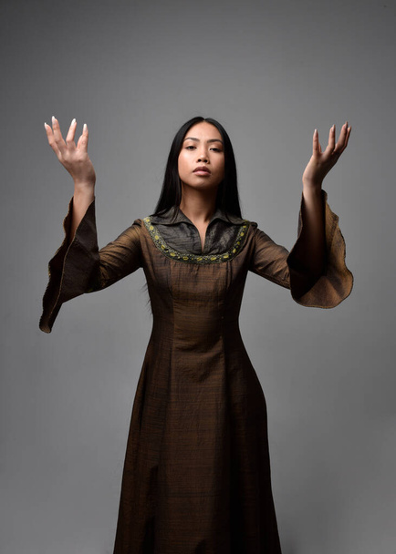 Close up portret pięknej młodej azjatyckiej kobiety z długimi włosami w średniowiecznej sukni fantasy. Pełna wdzięku pozycja z gestykulacyjnymi dłońmi, odizolowana na tle studia. - Zdjęcie, obraz