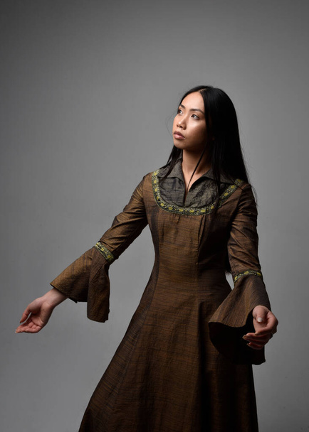Close-up portret van mooie jonge Aziatische vrouw met lang haar in middeleeuwse fantasiejurk. Genadige pose met gebaren handen, geïsoleerd op studio achtergrond. - Foto, afbeelding