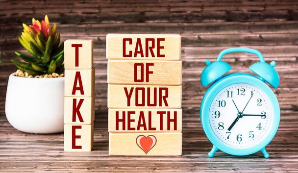 Take care of your health. The inscription is made on wooden blocks, next to a clock and a cactus flower on a wooden background - Zdjęcie, obraz