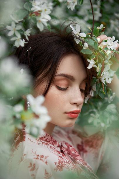 Woman with natural makeup, floral cosmetics for skin of the face, girl posing in flower branches of blooming apple tree in spring - Fotó, kép