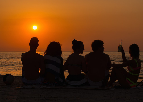 Silhouettes un jeune assis sur une plage regardant le coucher du soleil
  - Photo, image