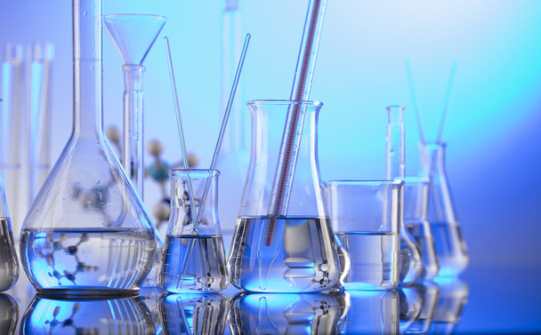 Laboratóriumi vizsgálatok. Üvegcsövek és kék hátterű főzőpoharak. - Fotó, kép