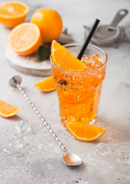 Aperol spritz summer cocktail in highball glass with oranges and strainer with bar spoon on light table background. Ice cubes and black straw. - 写真・画像
