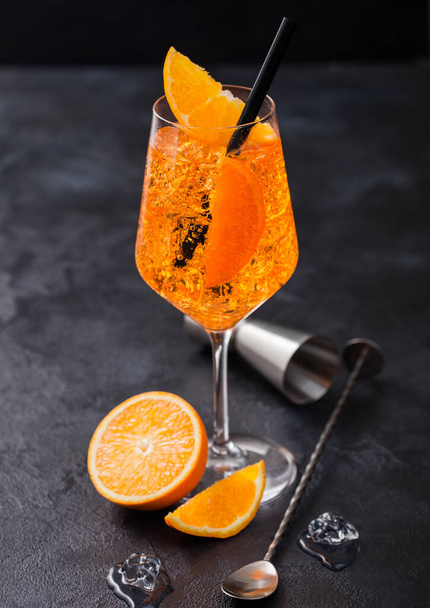 Glass of aperol spritz summer cocktail with orange slices and bar spoon with jigger on black background with ice cubes.  - Foto, Imagen