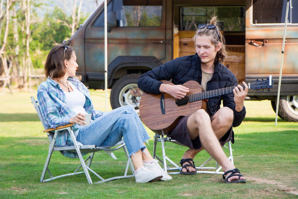 Jongeman en vrouw die plezier hebben en gitaar spelen en zingen terwijl de zomer vakantie kamperen. - Foto, afbeelding