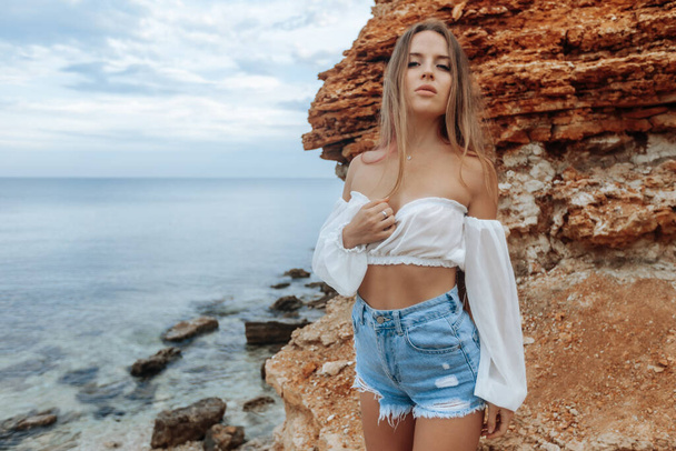 Sexy woman on a rocky beach in min shorts and a white blouse - Photo, Image