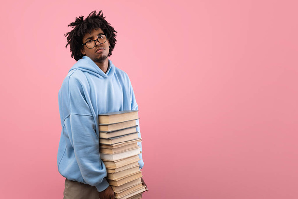 Depressiver und müder Afro-Teenager, der mit einem Stapel Bücher steht, nicht glücklich über Schulbeginn, Kopierraum - Foto, Bild