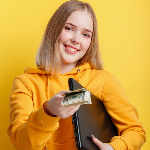 Beautiful smiling young woman freelancer with laptop take dollars money banknotes. IT remote freelancer remote worker via laptop isolated over yellow color background. Closeup square portrait - Foto, Imagen