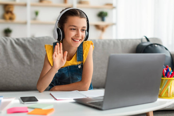 Girl in headphones using laptop, waving to webcam - Фото, зображення