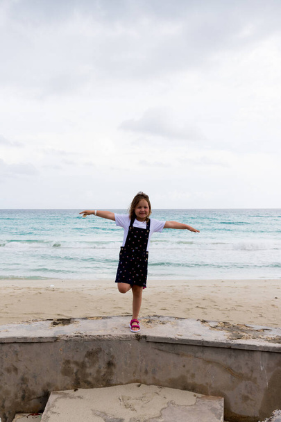 il bambino sta su una gamba, le braccia distese ai lati sullo sfondo del mare - Foto, immagini