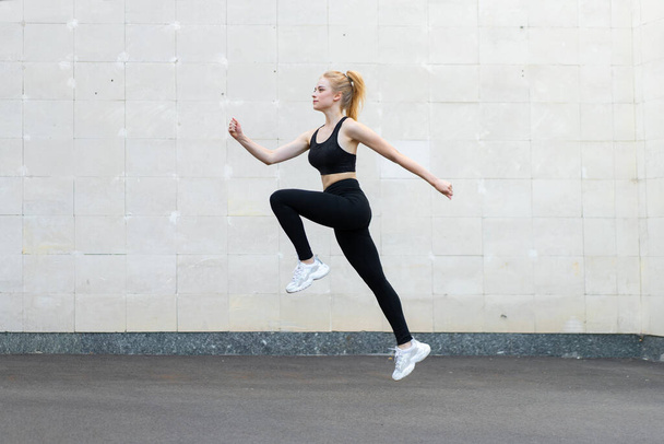 Sport and Fitness Concept Young Adult Caucasian Female Athlete Jumping High Outdoor Gray Tail Wall Background Sportive Woman Jump Exercises Outside Healthy Lifestyle Motivation - Foto, Bild