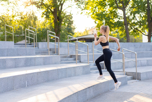Sport and Fitness. Fit Woman Running up stairs Summer Sunny Morning Caucasian Athletic Female Jogging Outdoor Cardio Training Active Healthy Lifestyle Dressed Black Sportswear Motivation Concept - Foto, afbeelding